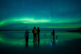 Photographers under the aurora on the reflecting beach